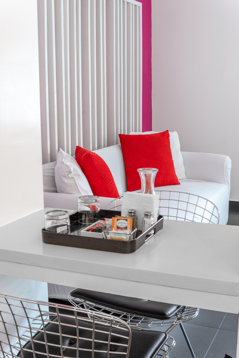 A tray with glasses and a carafe on a table in front of a white couch with red pillows.