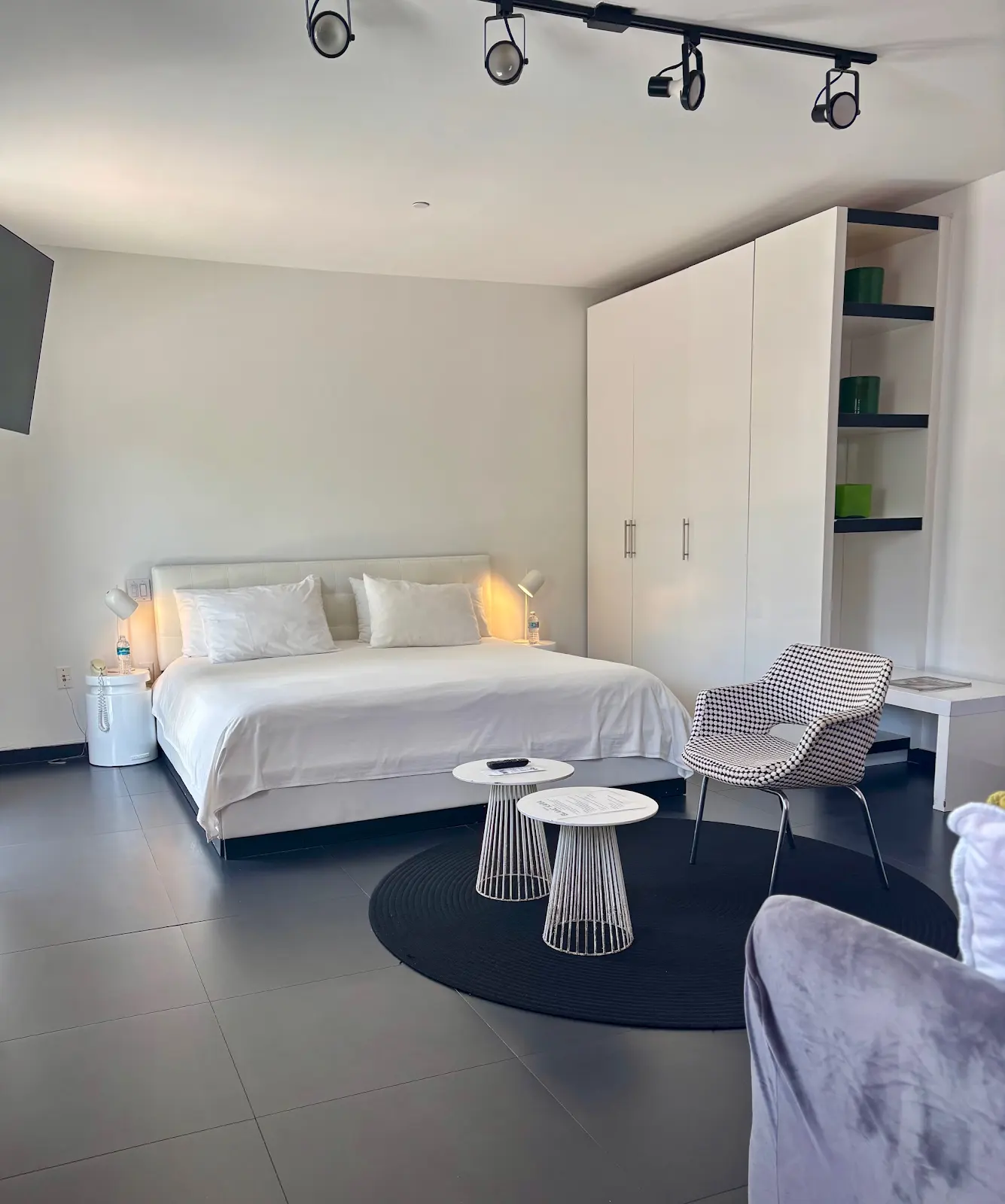A modern hotel room with a large bed, a black and white chair, and a small table.